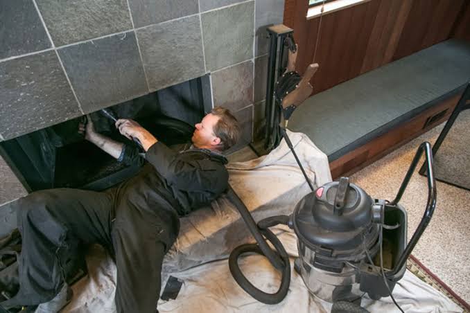 A person examining the inside of a fireplace with a vacuum positioned nearby
