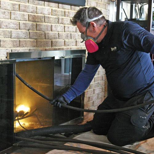 A person wearing a respirator working inside a brick fireplace
