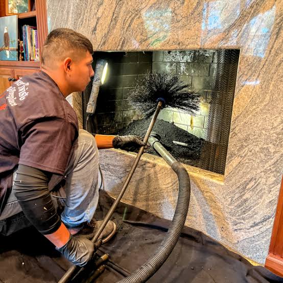 A person using a chimney brush inside a stone-surround fireplace