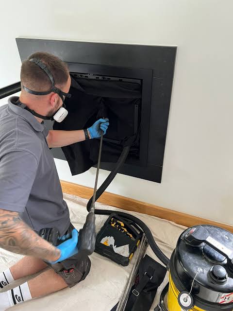 A person with cleaning equipment working at a black inset fireplace
