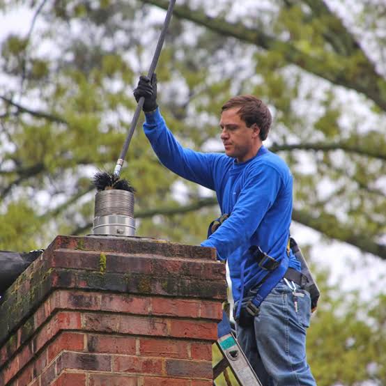 A weathered brick chimney with a metal flue and a person working nearby